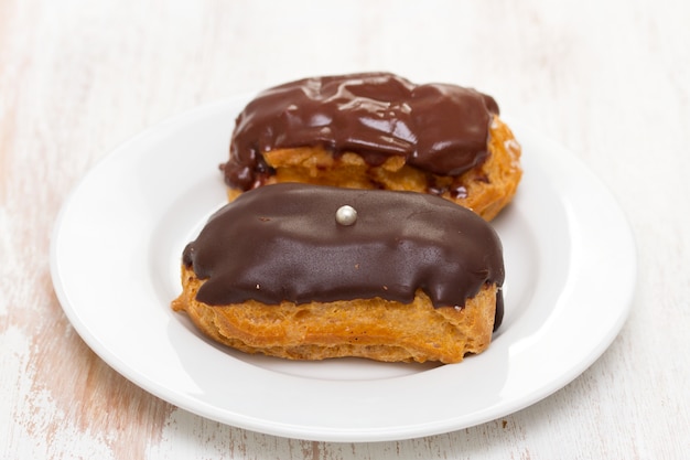 Eclairs di choclate sul piatto bianco su superficie di legno