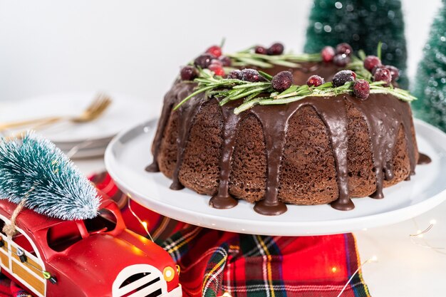 Chocolade bundt cake met chocolade frosting gedecoreerd met verse veenbessen en rozemarijn bedekt met een witte suiker.