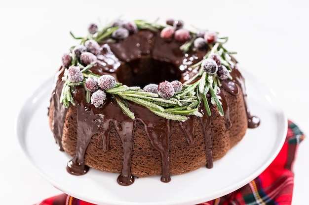 Chocolade bundt cake met chocolade frosting gedecoreerd met verse veenbessen en rozemarijn bedekt met een witte suiker.