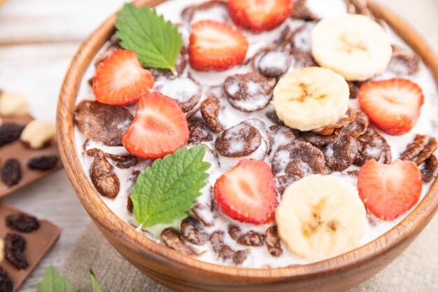 Chocolade cornflakes met melk en aardbei in houten kom op witte houten achtergrond Zijaanzicht selectieve focus