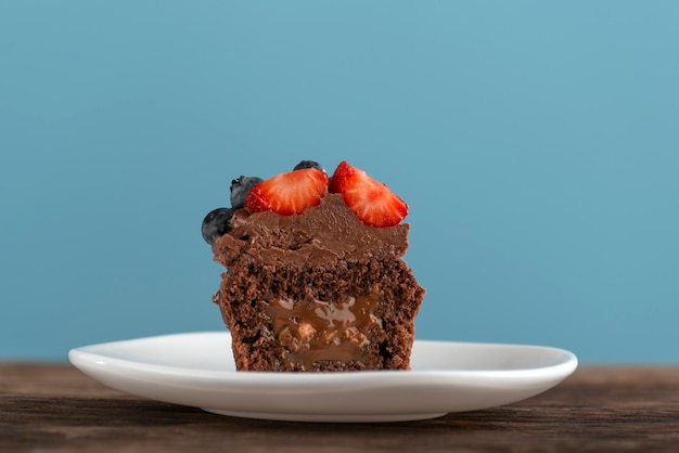 Chocolade cupcake met pure chocoladesuikerglazuur op houten tafel en blauwe achtergrond Chocolademuffin met karamelvulling