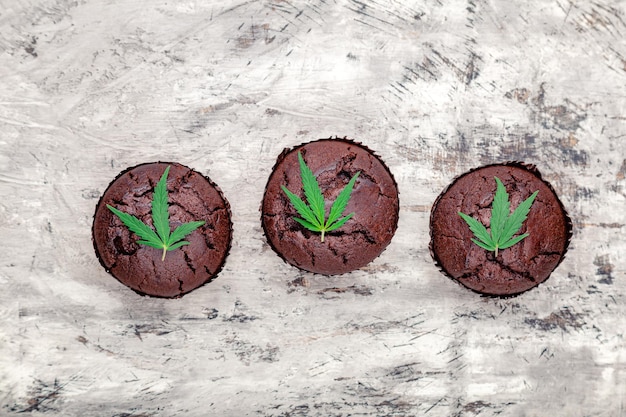 Chocolade cupcake muffins met wietbladeren wiet cbd. Medische marihuana-hennepmedicijnen in voedseldessert. Koken bakken wiet muffins met marihuana op grijze betonnen ondergrond. Bovenaanzicht.