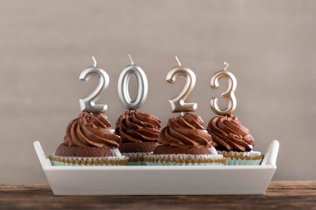 Chocolade cupcakes met buttercream frosting met zilveren 2023 kaarsen op houten tafel op lichtgrijze betonnen ondergrond