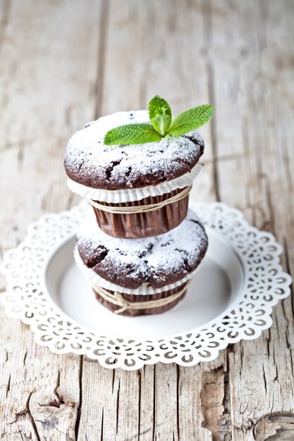 Chocolade donkere muffins met suiker poeder en muntblad op witte plaat op rustieke houten tafel.