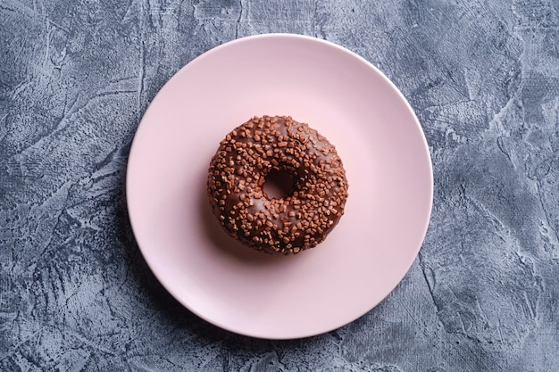 Chocolade donut met hagelslag op roze plaat, zoet geglazuurd dessertvoedsel op concrete gestructureerde achtergrond, bovenaanzicht