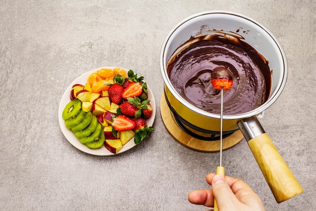 Chocolade fondue. Geassorteerd vers fruit, twee soorten chocolade, mannelijke hand. Ingrediënten voor het koken van een zoet romantisch dessert.