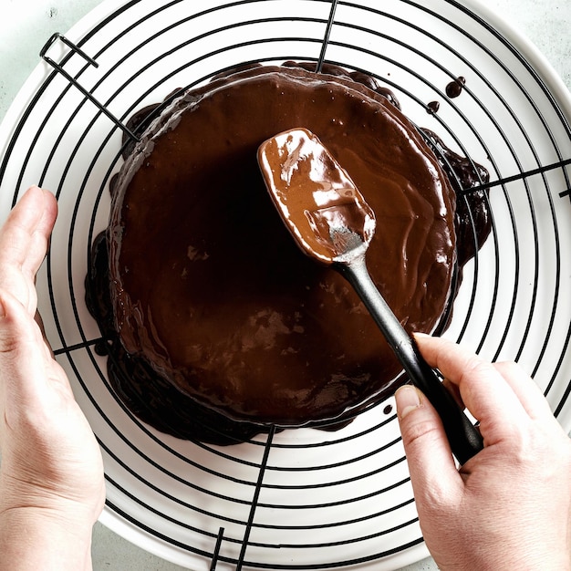 Chocolade ganache gieten op de taart vrouwelijke handen