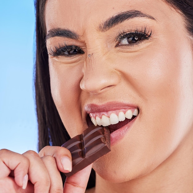 Chocolade gelukkig en portret van vrouw in studio die luxe zoete lekkernijen en snoep eet op blauwe achtergrond Suiker ongezond dieet en gezicht van vrouwelijke persoon met cacaoreep dessert en heerlijke snack
