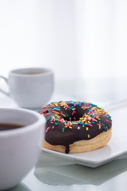Chocolade hagelslag donut op een witte plaat en een kopje koffie