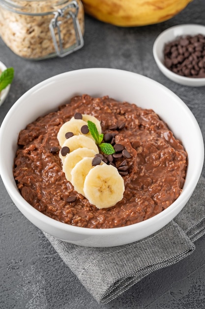 Chocolade havermoutpap met banaan en chocoladeschilfers bovenop in een witte kom Kopieer de ruimte