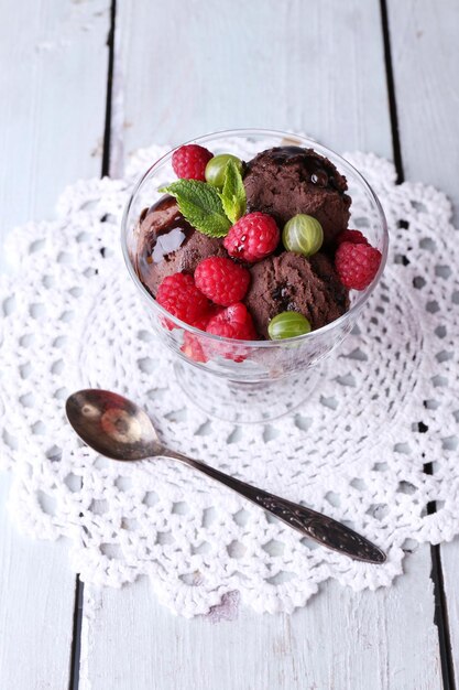 Chocolade-ijs met muntblad en rijpe bessen in glazen kom op een houten achtergrond kleur