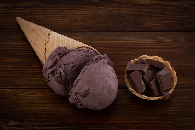 Chocolade-ijs scoops in wafel kegels en chocolade stukjes op houten achtergrond.