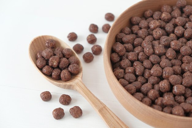 Chocolade maïs ballen in een houten kom en lepel verspreid op een witte achtergrond