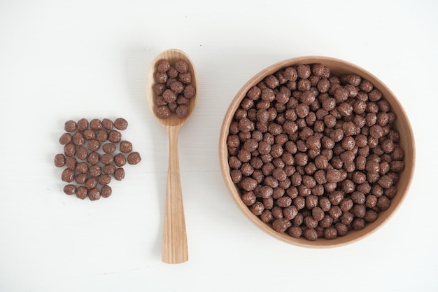 Chocolade maïs ballen in een houten kom en lepel verspreid op een witte achtergrond