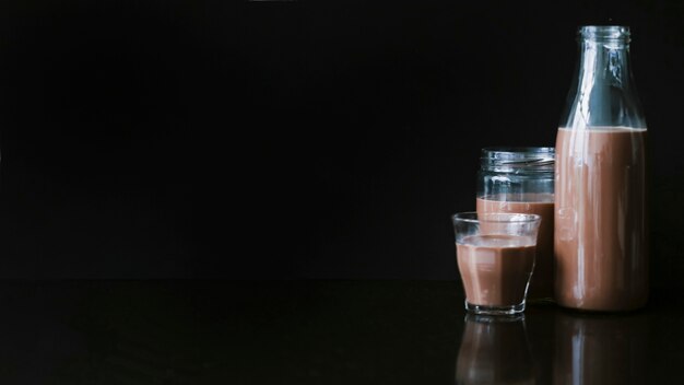 Chocolade milkshake in de pot; glas en fles op zwarte achtergrond