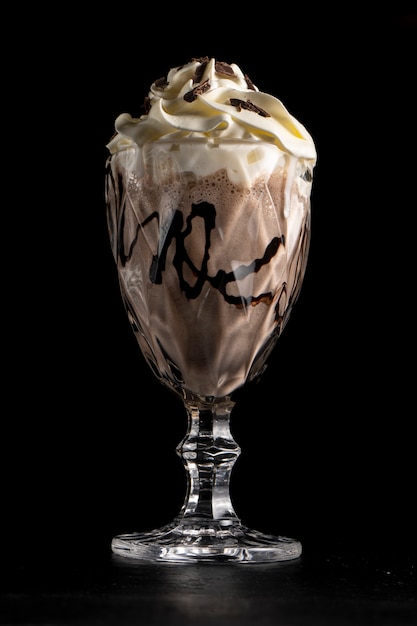 Chocolade milkshake met chocolade en room in een glas op een zwarte achtergrond.