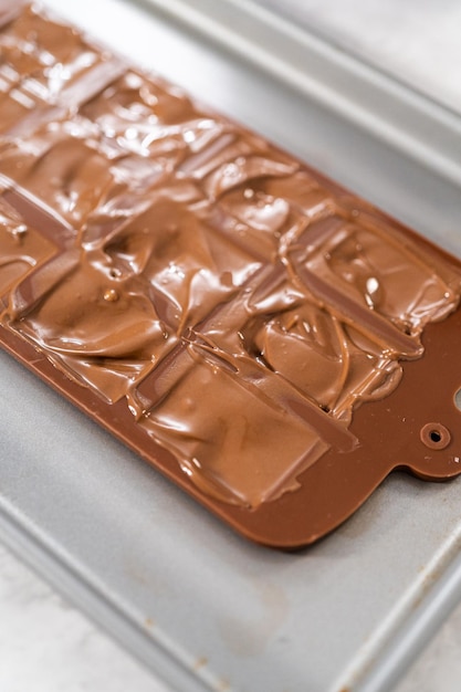 Chocolade-siliconenvorm vullen met gesmolten donkere chocolade om gastronomische mini-pralines met hagelslag te bereiden