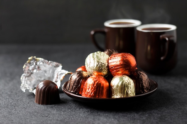 Chocolade snoepjes verpakt in veelkleurige folie en twee kopjes koffie op zwarte ondergrond