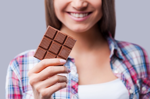 Chocolade stemming. Close-up van jonge vrouwen die een reep chocolade vasthouden en glimlachen terwijl ze tegen een grijze achtergrond staan