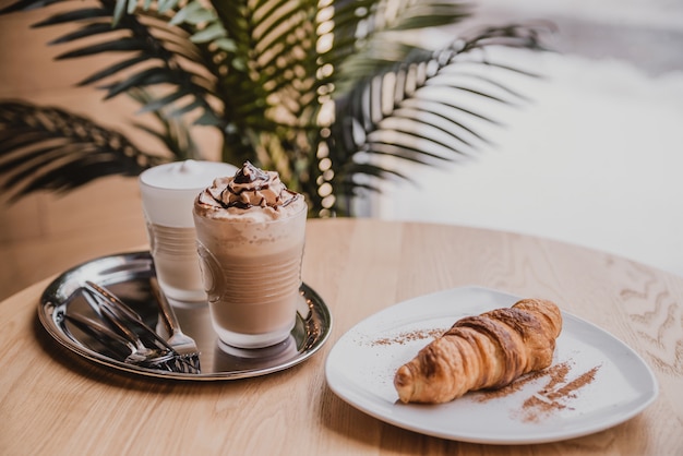 Chocoladecocktail met ijs. cappuccino en croissant in het café. koffie in de ochtend, ontbijt in een gezellig café bij het raam