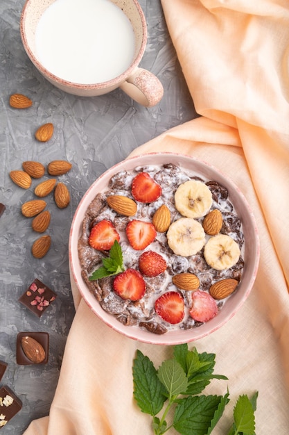 Chocoladecornflakes met melkaardbei en amandelen in keramische kom op grijze betonnen achtergrond Bovenaanzicht close-up