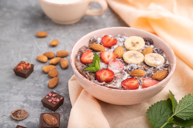 Chocoladecornflakes met melkaardbei en amandelen in keramische kom op grijze betonnen achtergrond Zijaanzicht selectieve focus