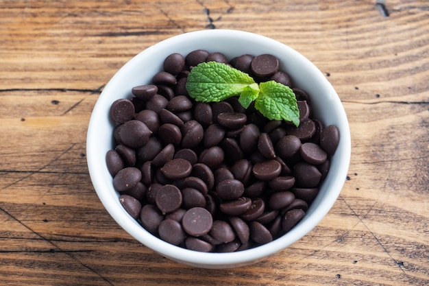 Chocoladedruppels voor het decoreren van desserts in een bord met munt op een houten tafel.