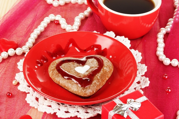 Chocoladekoekje in de vorm van een hart met een kopje koffie op een roze tafelkleedclose-up