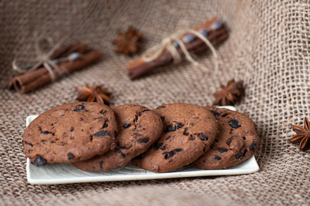 Chocoladekoekjes liggen op een witte schotel op een zak, kaneel en steranijs. Bakkerijproducten