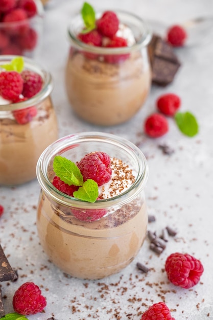 Chocolademousse met slagroom en verse frambozen in een glas op een grijze betonnen ondergrond