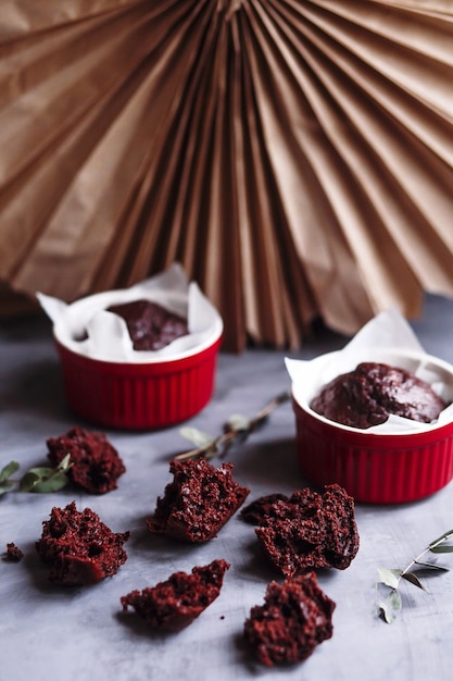 Chocolademuffins in rode kopjes. Kleine geglazuurde keramische ramekin met bruine cakes op een grijze en witte achtergrond.