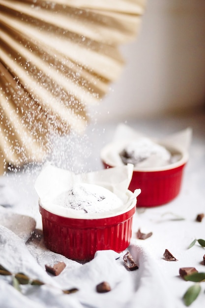 Chocolademuffins in rode kopjes. Kleine geglazuurde keramische ramekin met bruine cakes op een grijze en witte achtergrond.