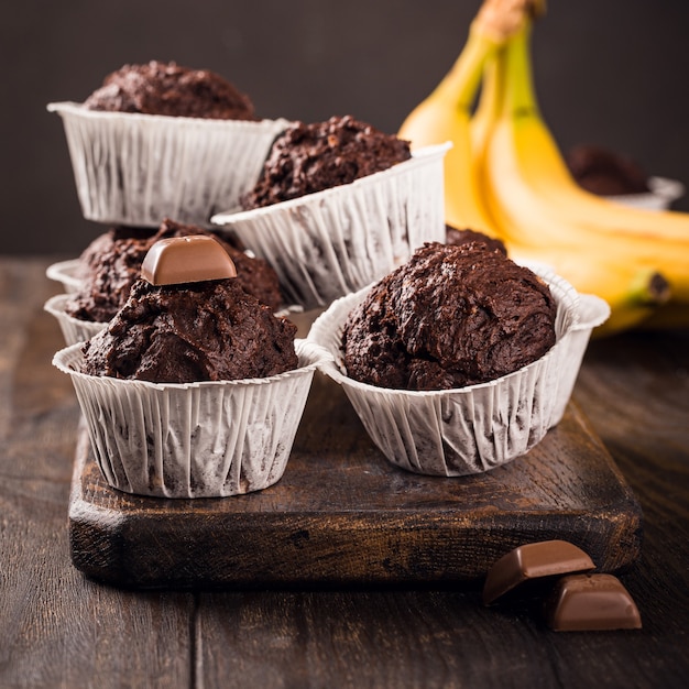 Chocolademuffins met banaan in witte papieren bekers op donkere houten ondergrond. Feest eten concept