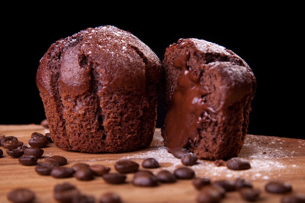 Chocolademuffins met chocolade en koffiebonen en suiker op een houten lijst en een zwarte achtergrond.