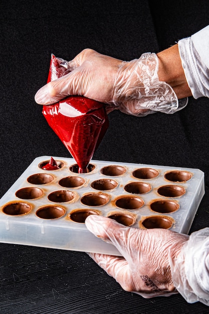 chocoladeproducent knijpt in de tube met aardbeienroom om de bonbons in de vorm te vullen
