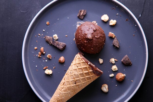 Chocoladeroomijs met hazelnoten in een hoorntje op een donker bord