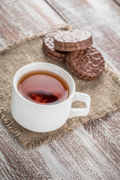 Chocoladeschilferkoekjes en een mok thee op witte houten lijst.