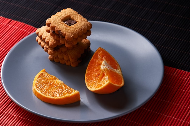 Foto chocoladeschilferkoekjes en stuk van sinaasappel op plaat en op rood en zwart