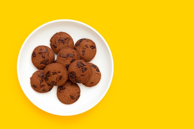 Chocoladeschilferkoekjes in witte plaat op gele achtergrond.