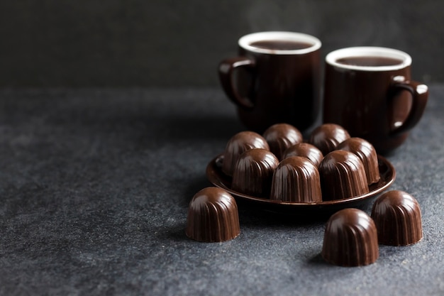 Chocoladesuikergoed op een bord en twee kopjes warme koffie op zwarte achtergrond met kopieerruimte