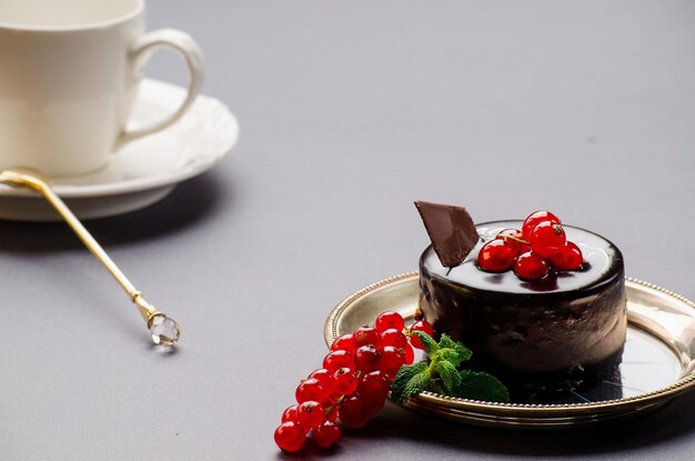 Chocoladetaart met rode aalbessen witte kop met schotel en lepel op een grijze achtergrond