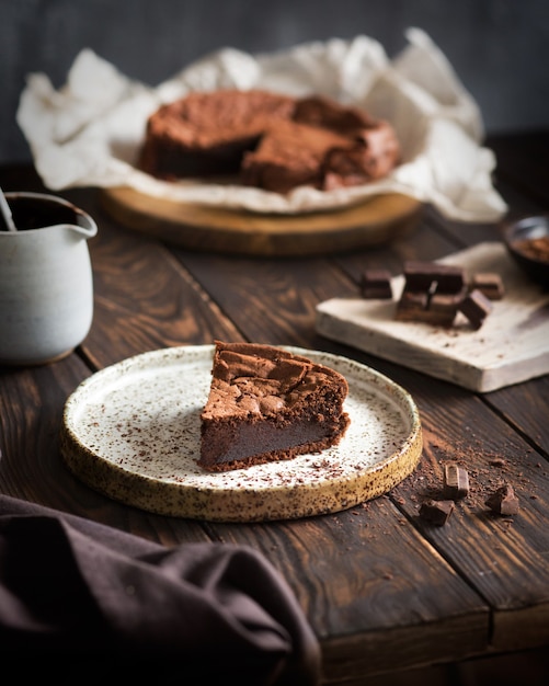 Chocoladetaart op een houten tafel Een stuk brownie op een bruine achtergrond Cacao en chocoladestukjes