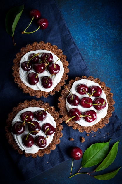 Chocoladetaartjes met room en verse bessen van zoete kers op een donkere betonnen tafel. Selectieve aandacht. Bovenaanzicht.