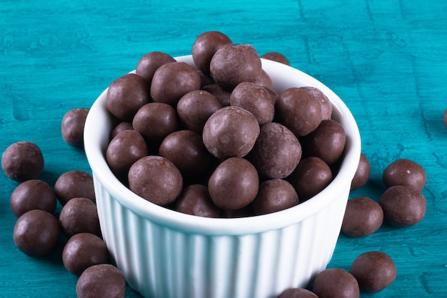 Chocolate balls in white bowl on blue surface.