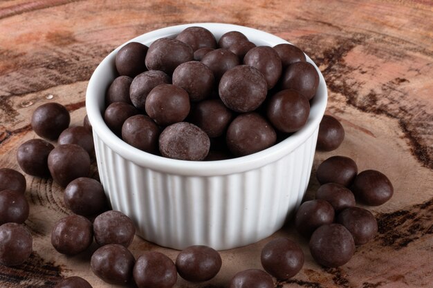 Chocolate balls in white bowl on wooden surface.