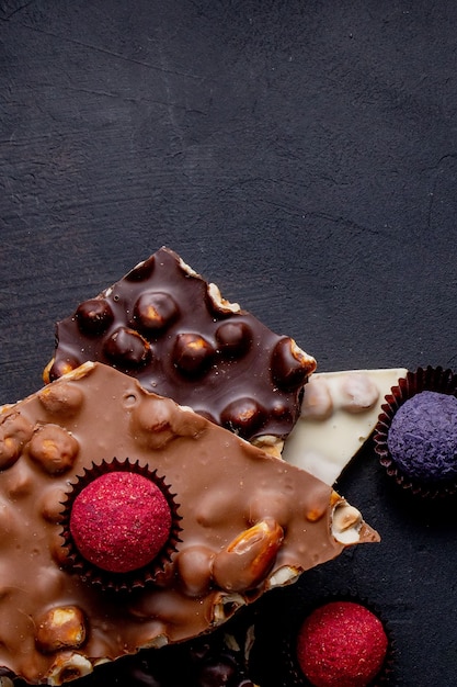 Плитка шоколада, измельченные кусочки темного шоколада и орехи. Пралине Шоколадные конфеты.