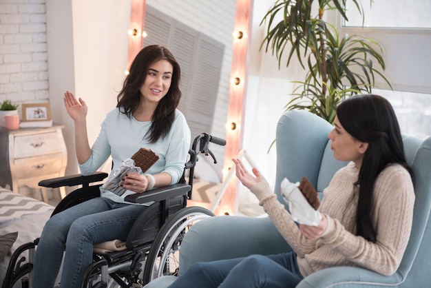 Chocolate bar. Glad disabled woman and friend tasting chocolate bar and chatting