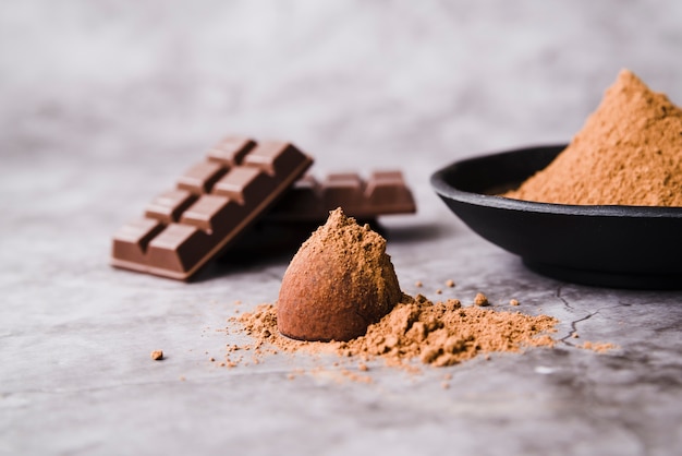 Chocolate bar and truffle coated cocoa powder on concrete backdrop