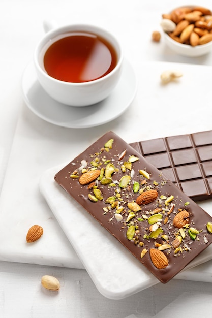 Chocolate bar with almond and pistachios on a white board two chocolate bars sweets with tea