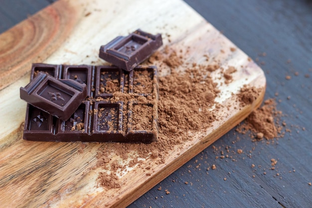 Chocolate bar with scattered cocoa powder on the wooden board